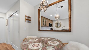 A dining area with a round table, chairs, a chandelier, and a mirror reflecting the kitchen. - The Jewel Box - Fully Updated Downtown Condo w/ AC (Sandpoint)