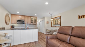 A modern kitchen with white cabinets, a central island, and a dining area with a round table. - The Jewel Box - Fully Updated Downtown Condo w/ AC (Sandpoint)