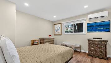 A bedroom with a bed, a dresser, a bench, a window, and artwork on the walls.