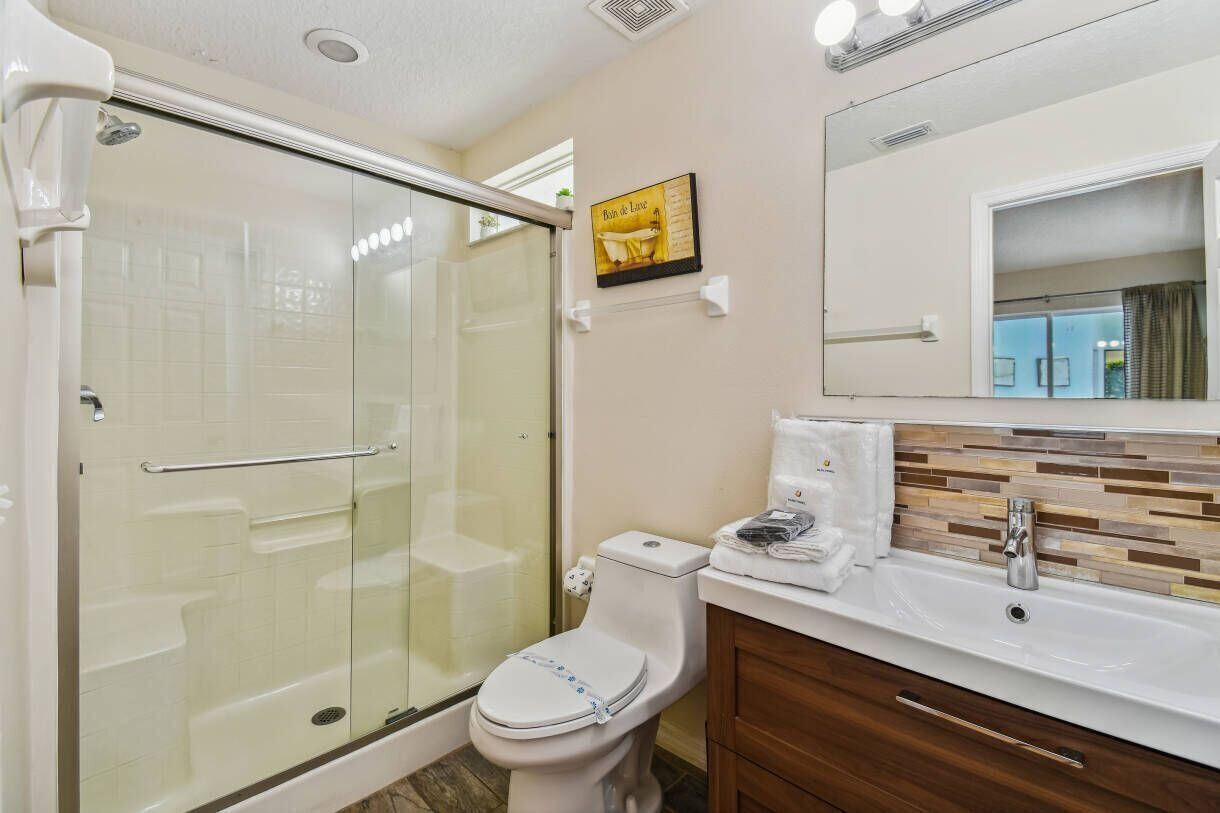 A bathroom with a glass-enclosed shower, a toilet, a sink with a mirror, and a tiled backsplash.
