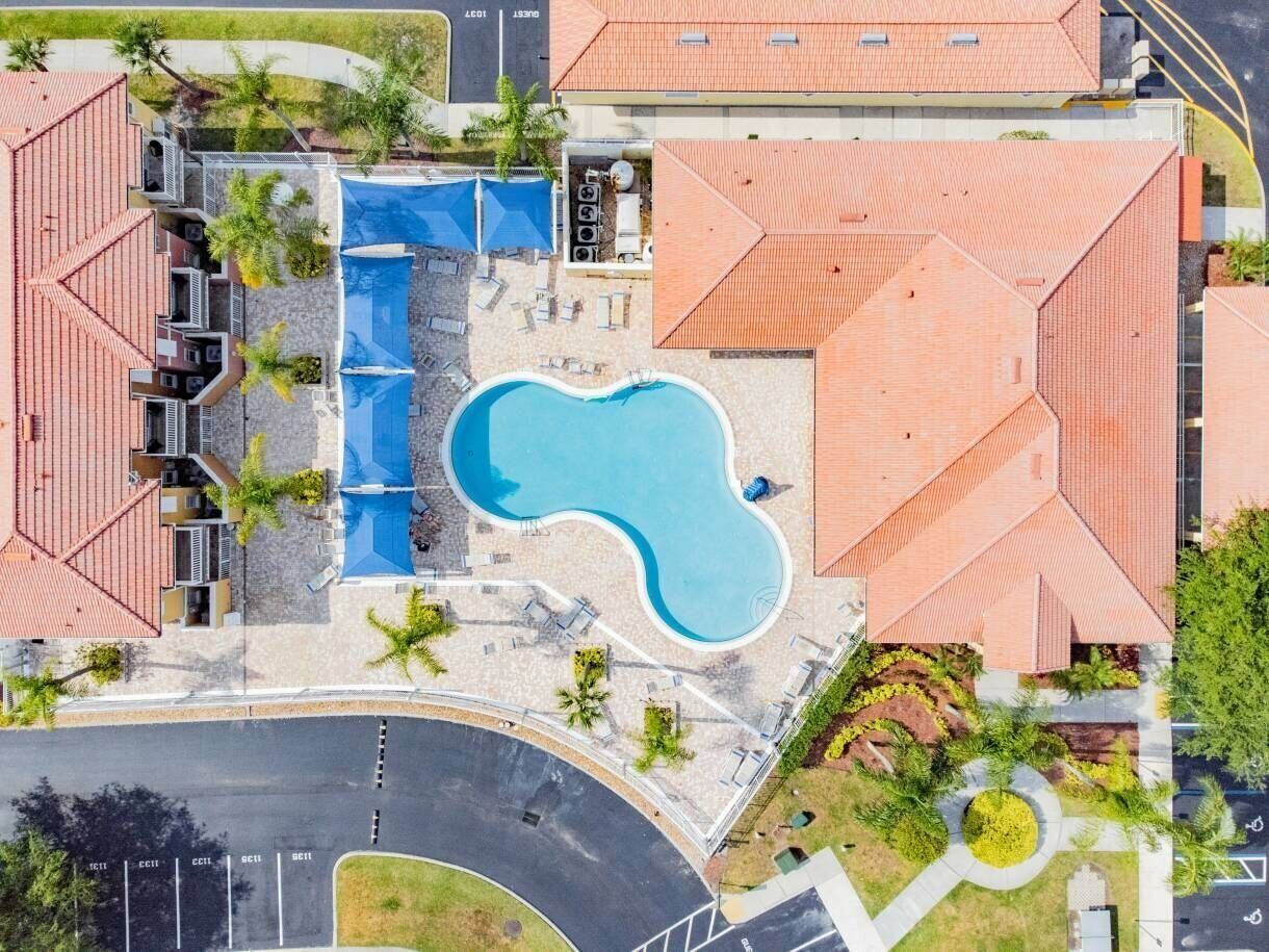An aerial view of a hotel with a swimming pool, multiple buildings with red roofs, and a parking area.