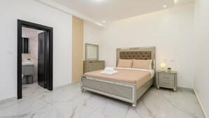 Un dormitorio con cama, mesitas de noche, un espejo y una puerta que da al baño.