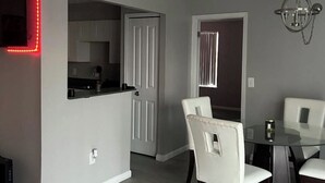 A modern kitchen with white cabinets, a black countertop, and a red LED light strip. There is a dining area with a glass table and white chairs. - Charming 2-bedroom apartment with fitness room and AC in Southfield (Southfield)