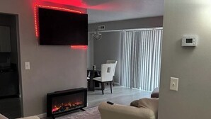 A modern living room with a flat-screen TV, a fireplace, and a red LED light strip on the ceiling. - Charming 2-bedroom apartment with fitness room and AC in Southfield (Southfield)