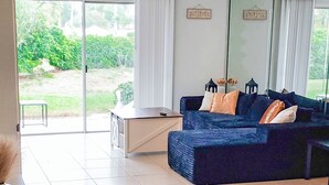 Ein geräumiger Wohnbereich mit einem großen, blauen Sofa, einem weißen Couchtisch und Blick auf einen Garten durch eine Schiebetür.