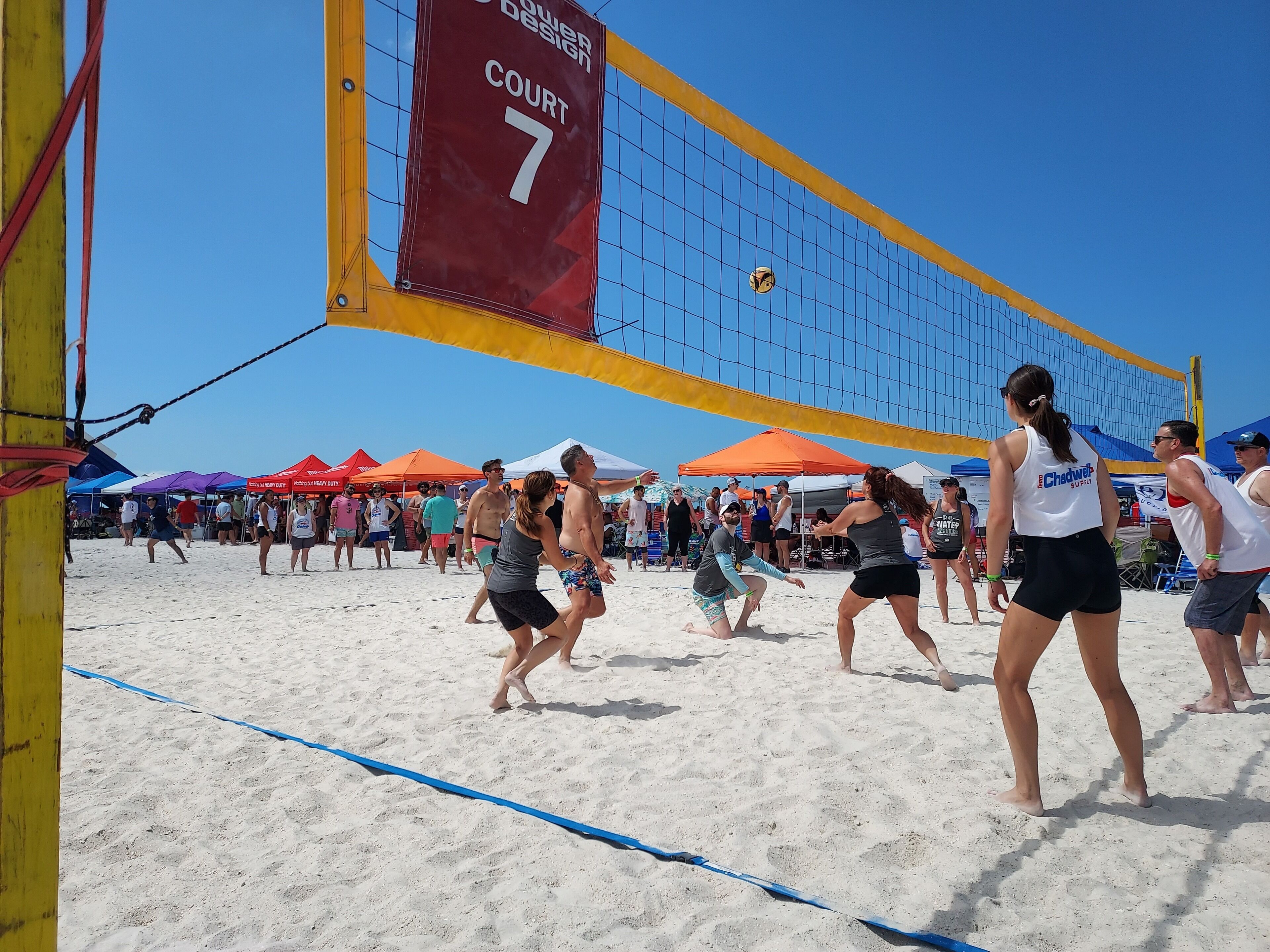 A beach volleyball court with a net, sand, and people playing.