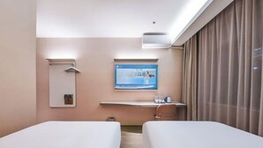 Une chambre d’hôtel avec deux lits, un bureau doté d’un écran d’ordinateur, une petite table avec une cafetière et une fenêtre avec des rideaux.