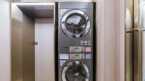 Un espace buanderie compact et moderne, équipé de deux machines à laver superposées, de panneaux de commande et d’une finition en acier inoxydable.