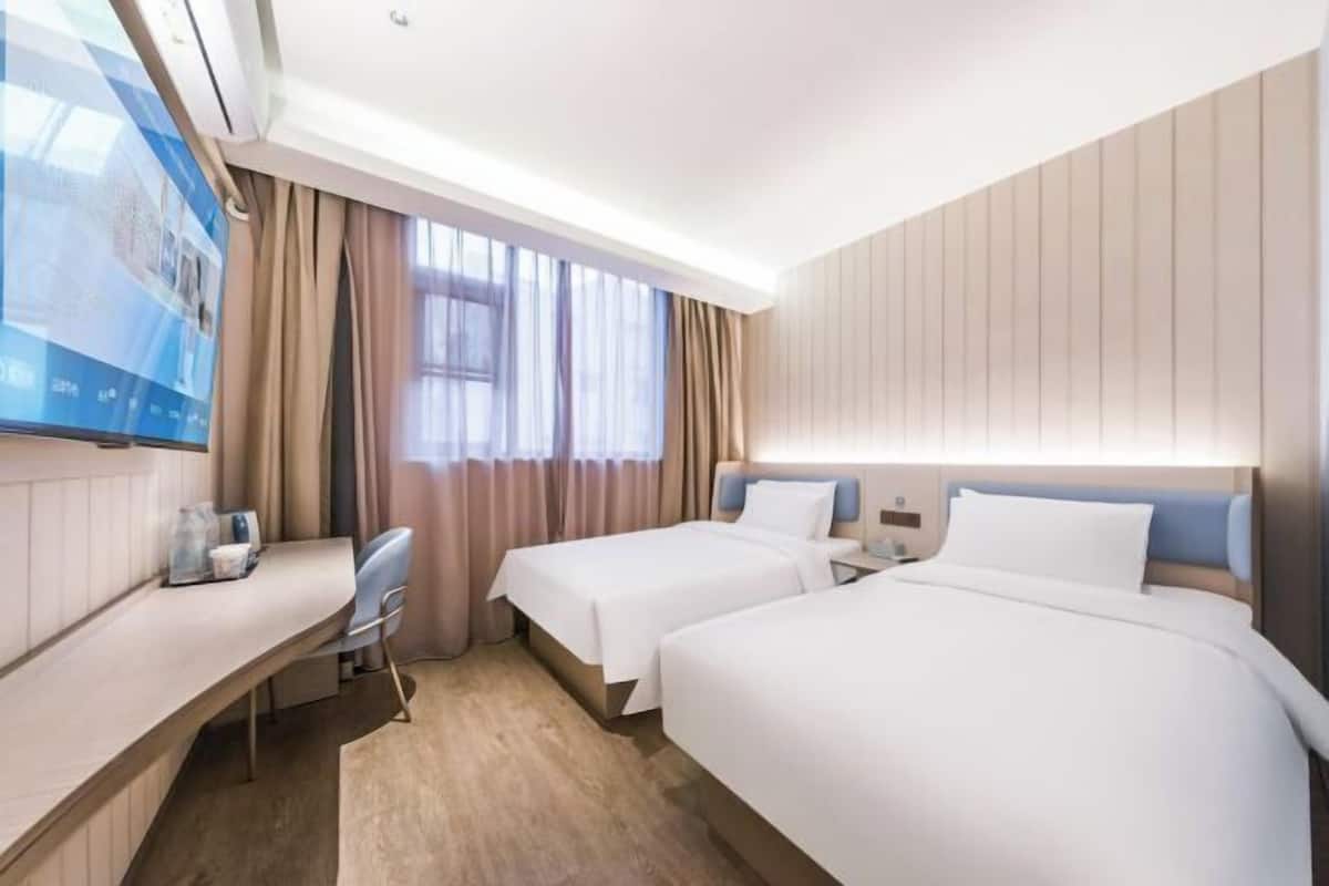 A hotel room with two beds, a desk, a TV, and a window with curtains.