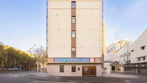Un hôtel à plusieurs étages, doté d’une façade sobre, d’une entrée bien visible et surplombant un ciel dégagé.