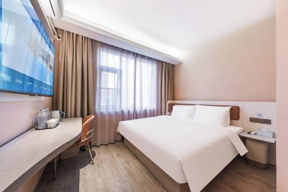 A hotel room with a bed, a desk, a chair, a TV, and a window with curtains.