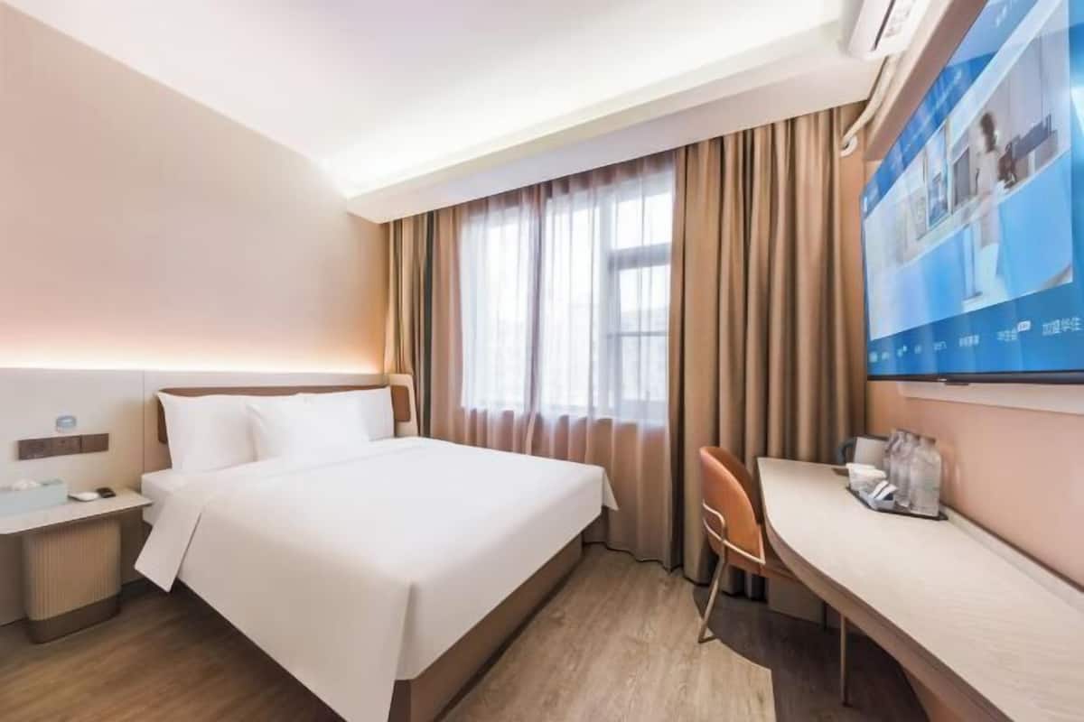 A hotel room with a bed, a desk, a chair, a TV, and curtains.
