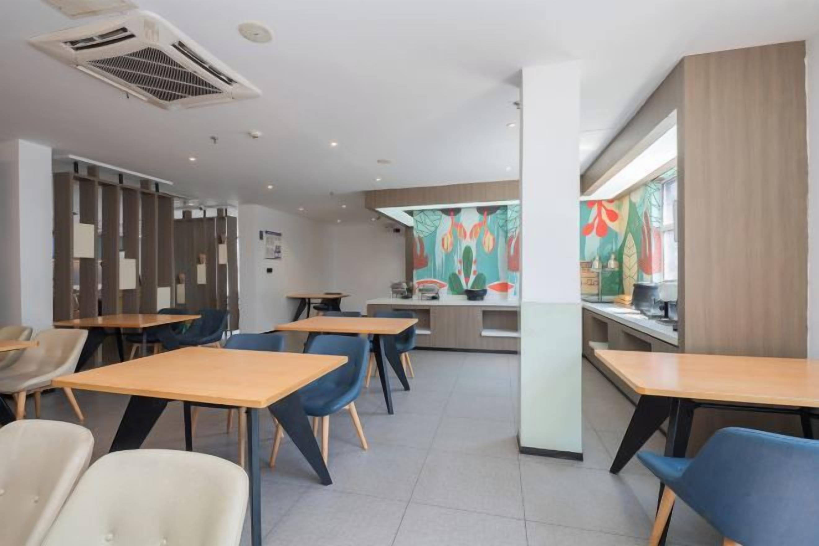 En moderne restaurant med borde, stole, et køkkenområde og et farverigt mural på væggen.