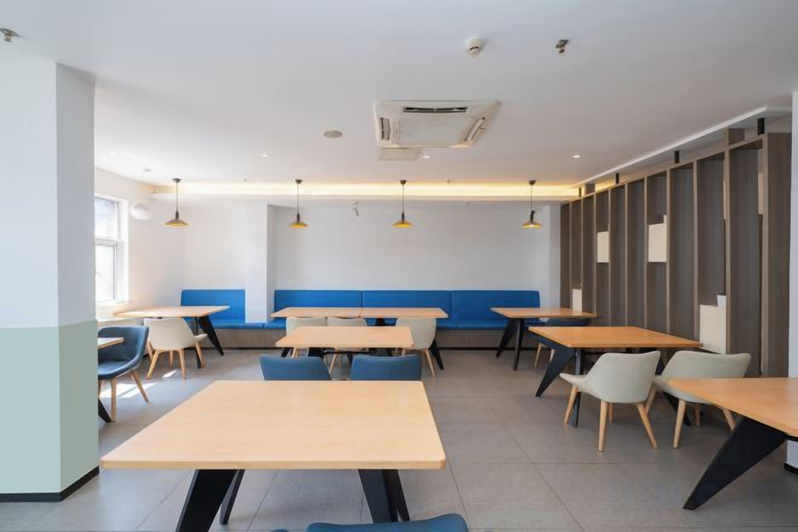 A modern dining area with tables and benches, a blue accent wall, and pendant lighting.