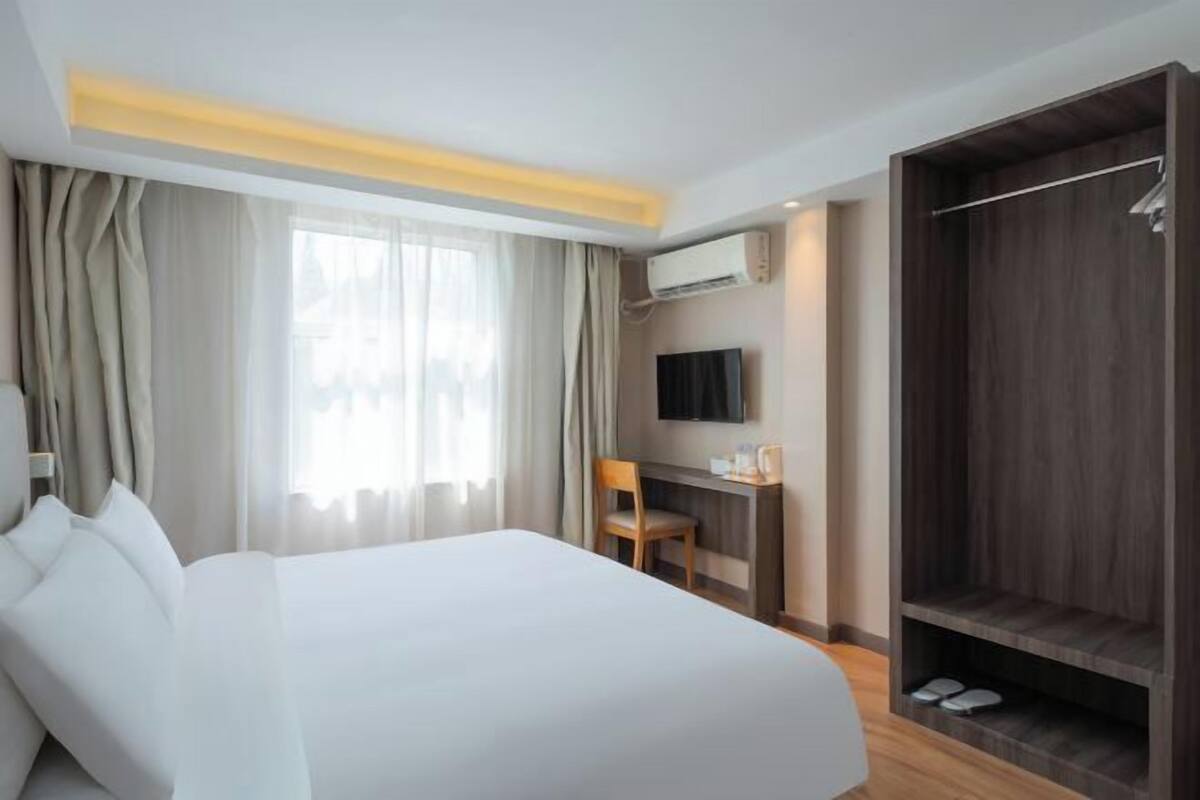 A hotel room with a bed, a desk, a TV, an air conditioning unit, and a wardrobe.