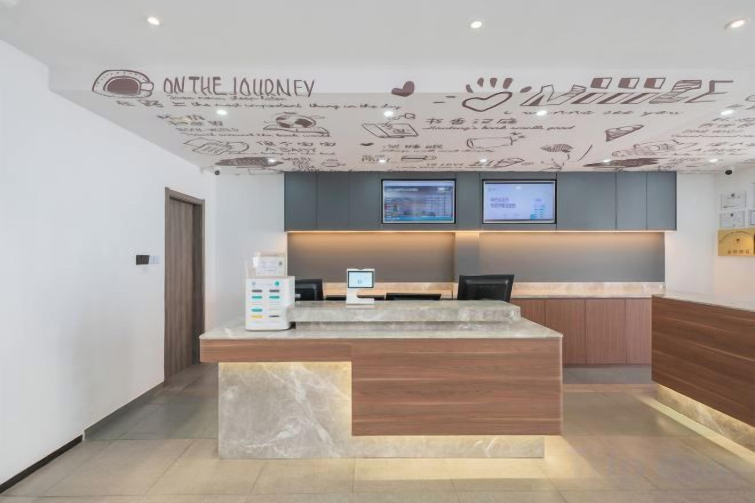 A reception desk with a digital screen, a coffee machine, and a wall with a travel-themed mural.