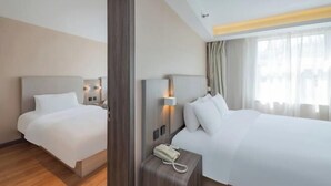 A hotel room with two beds, a bedside table with a phone, and a window with curtains.
