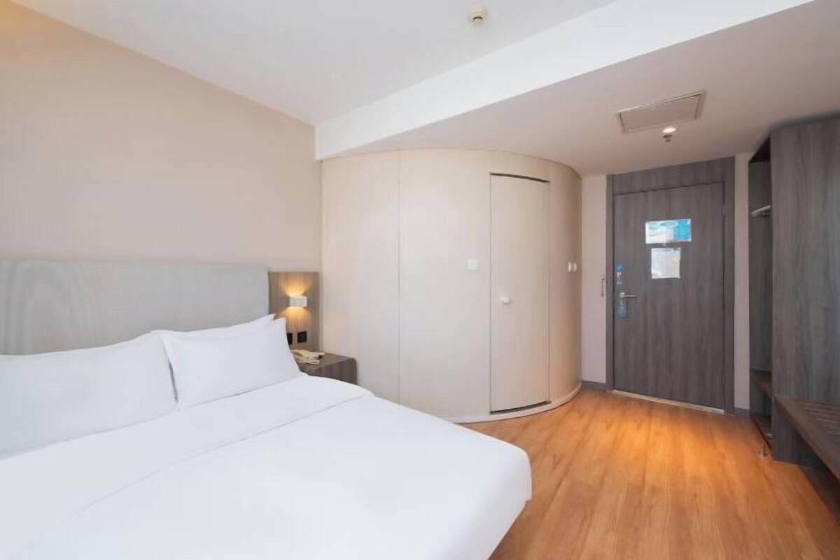 A hotel room with a bed, a wardrobe, a nightstand, and a door with a sign.