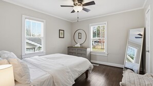 A bedroom with a bed, a dresser, a ceiling fan, and two windows.