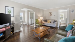 A living room with a wooden coffee table, a sofa, a TV, and a kitchen area in the background.