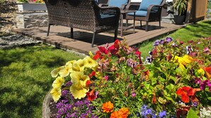 A patio with wicker furniture and a flower bed with various flowers.