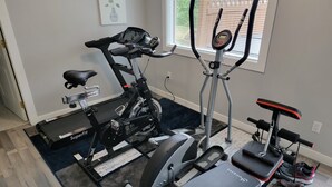 A home gym with an elliptical, a stationary bike, a bench, and a treadmill.