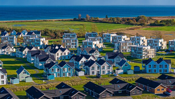 Een woongebied aan de kust met moderne huizen, helder uitzicht op zee en een golfbaan op de achtergrond.