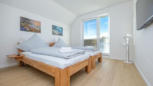 Een moderne slaapkamer met twee bedden, houten hoofdborden, een groot raam met zonwering en kunst aan de wand.