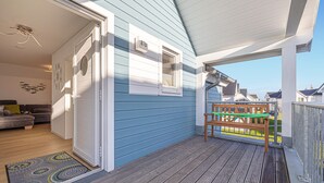 Een blauw huis met een houten terras, een deur en een raam.