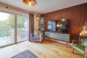 Ein geräumiges Wohnzimmer mit einem großen Fernseher, einer Holzkommode und einem Sessel.