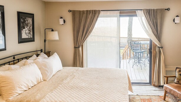 A hotel room with a large bed, a desk, a chair, a lamp, and a view of the outdoor deck. - First Floor Slopeside Ski-in / Ski-out at Wintergreen, steps from main lodge (Wintergreen Resort)