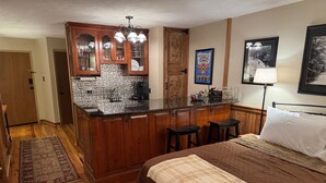 A compact hotel room with a kitchenette, a bed with a brown quilt, a patterned rug, and a framed picture on the wall. - First Floor Slopeside Ski-in / Ski-out at Wintergreen, steps from main lodge (Wintergreen Resort)