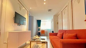 A modern living room with a red sofa, a glass coffee table, and a TV mounted on the wall.