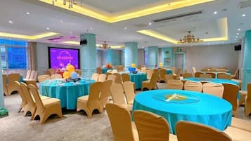A banquet hall with round tables, chairs, and a stage with a screen.