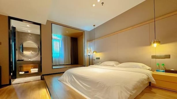 A modern hotel room with a large bed, a round mirror, and a view of the outdoors.
