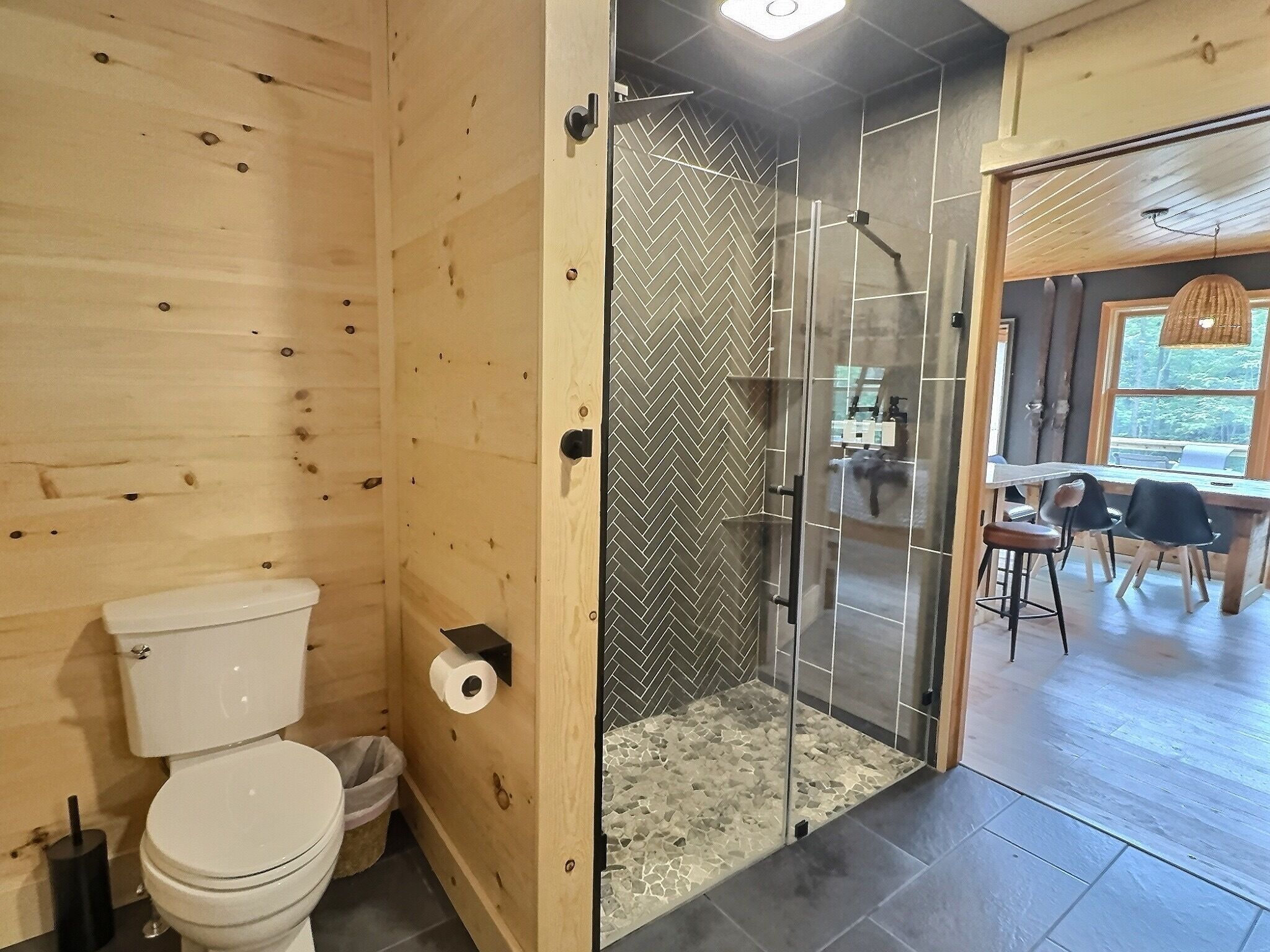 Un interior de madera con ducha envuelta en cristal, inodoro y un pequeño cubo de basura.