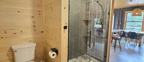 Un interior de madera con ducha envuelta en cristal, inodoro y un pequeño cubo de basura.