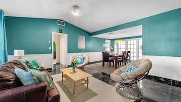 Una sala de estar con paredes azul verdoso, un sofá de cuero marrón, una mesa de centro de madera y un comedor con una mesa y sillas.