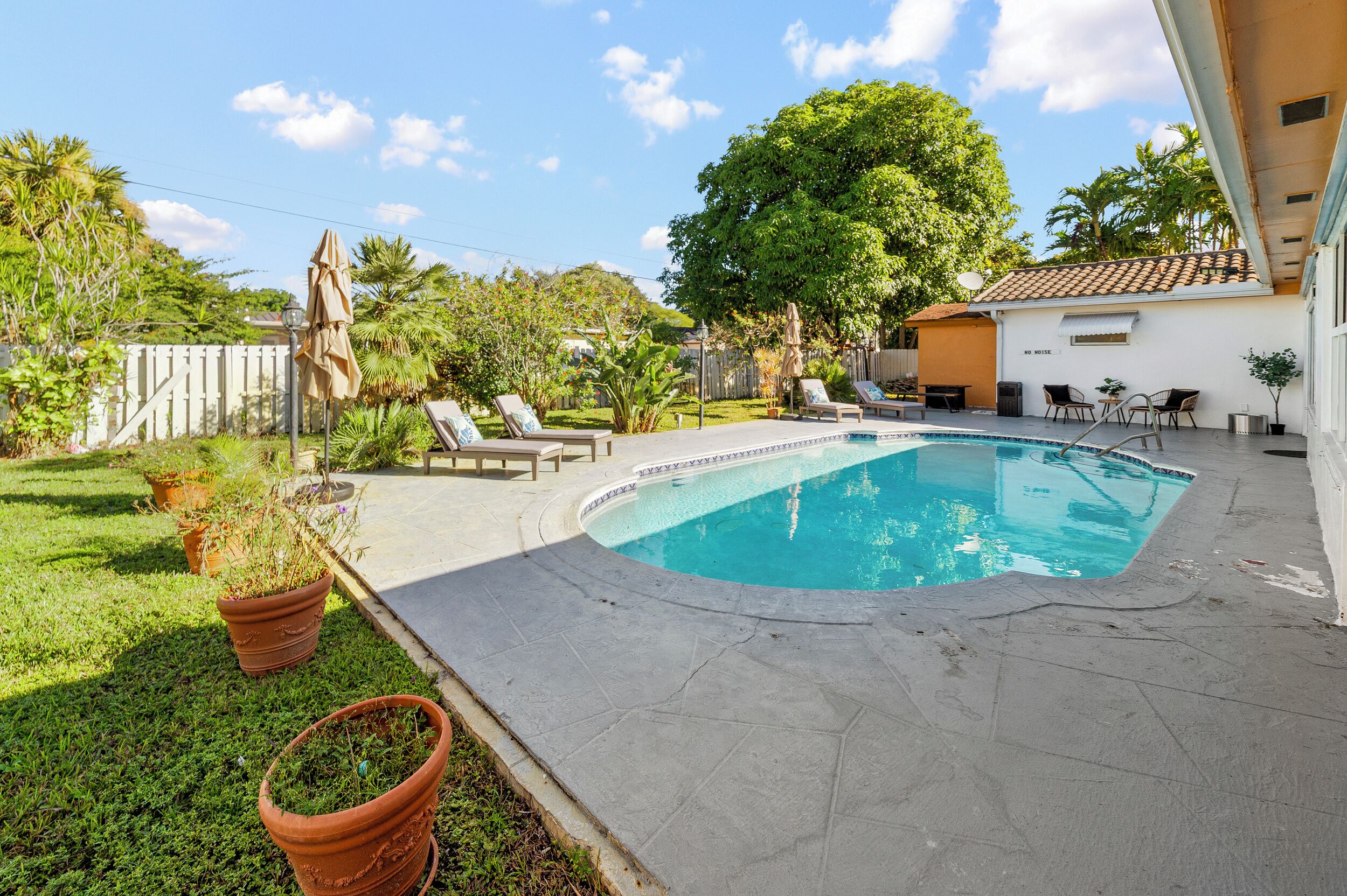 Um quintal com piscina, cadeiras de sol e vasos de plantas.