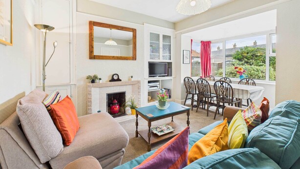 A living room with a sofa, a coffee table, a fireplace, a TV, and a dining area with chairs and a table. - Host Stay Highgarth (Seahouses)