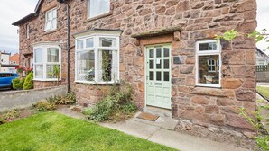 A stone house with a green door, white-framed windows, and a small garden. - Host Stay Highgarth (Seahouses)