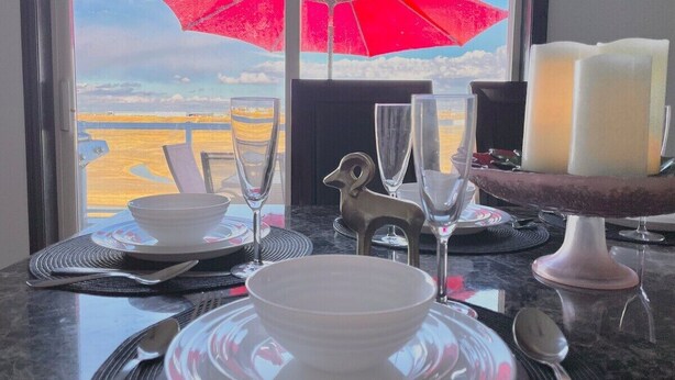 A dining table set with white plates, bowls, and cutlery, a red umbrella, and a candle holder. - Covington Close (Calgary)