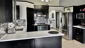 A modern kitchen with a central island, stainless steel appliances, black cabinetry, and a tiled backsplash. - Covington Close (Calgary)