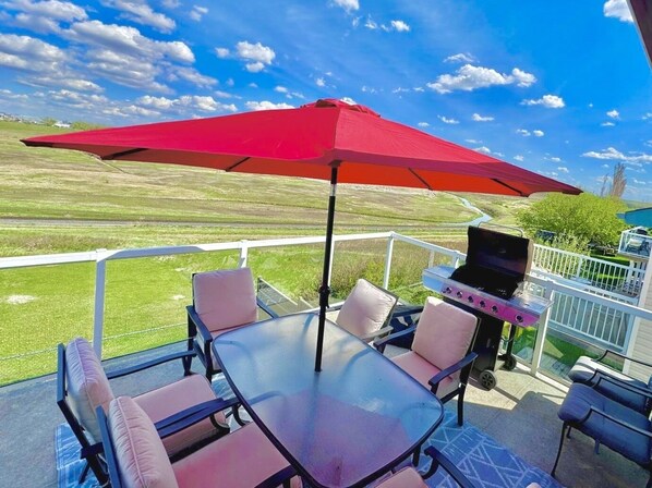 A patio with a glass table, chairs, a grill, and a red umbrella. - Covington Close (Calgary)