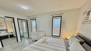 A bedroom with a large bed, a crib, and a mirror. - Covington Close (Calgary)