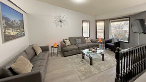 A modern living room with a sofa set, a glass coffee table, and a decorative wall piece. - Covington Close (Calgary)