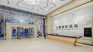 A modern hotel lobby with a reception desk, glass doors, and a large wall with text. - Anqing Yixin Hotel (Anqing)