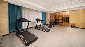 A spacious room with three treadmills aligned against a wall with teal and white curtains. - Anqing Yixin Hotel (Anqing)