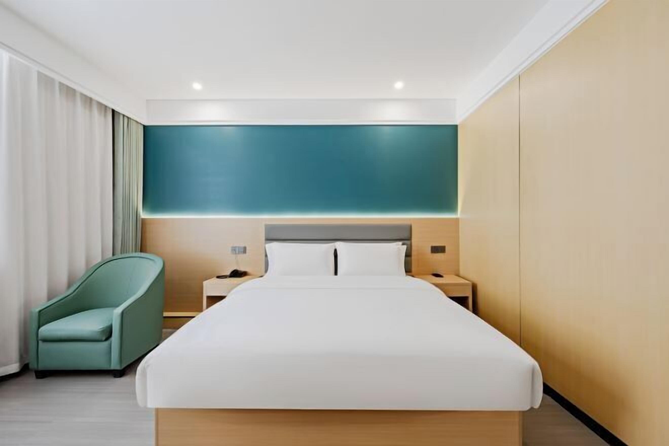 A modern hotel room with a large bed, a nightstand, a lamp, and a chair.