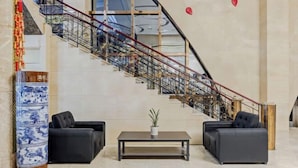 A lobby with a staircase, two black sofas, a small table with a plant, and a decorative vase. - Anqing Yixin Hotel (Anqing)